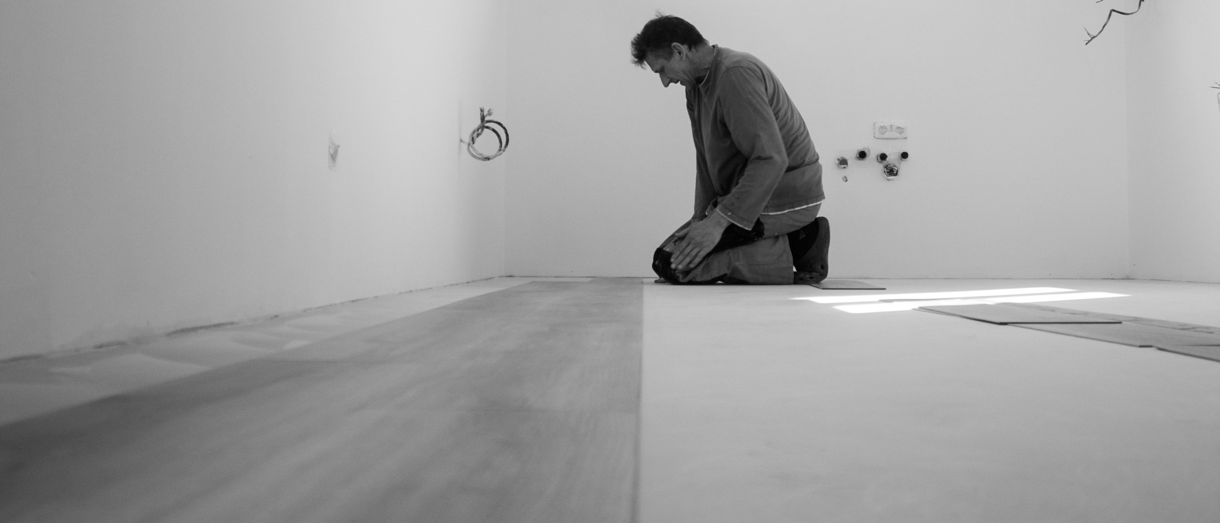 An installer kneeling to lay vinyl planks in an empty room.