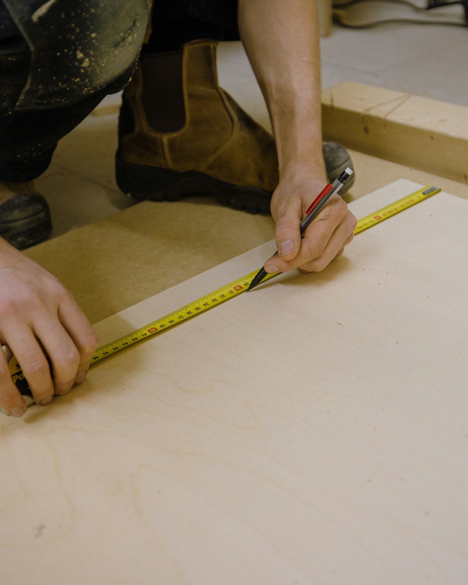 A contractor marking a board with a pencil and a tape measure.