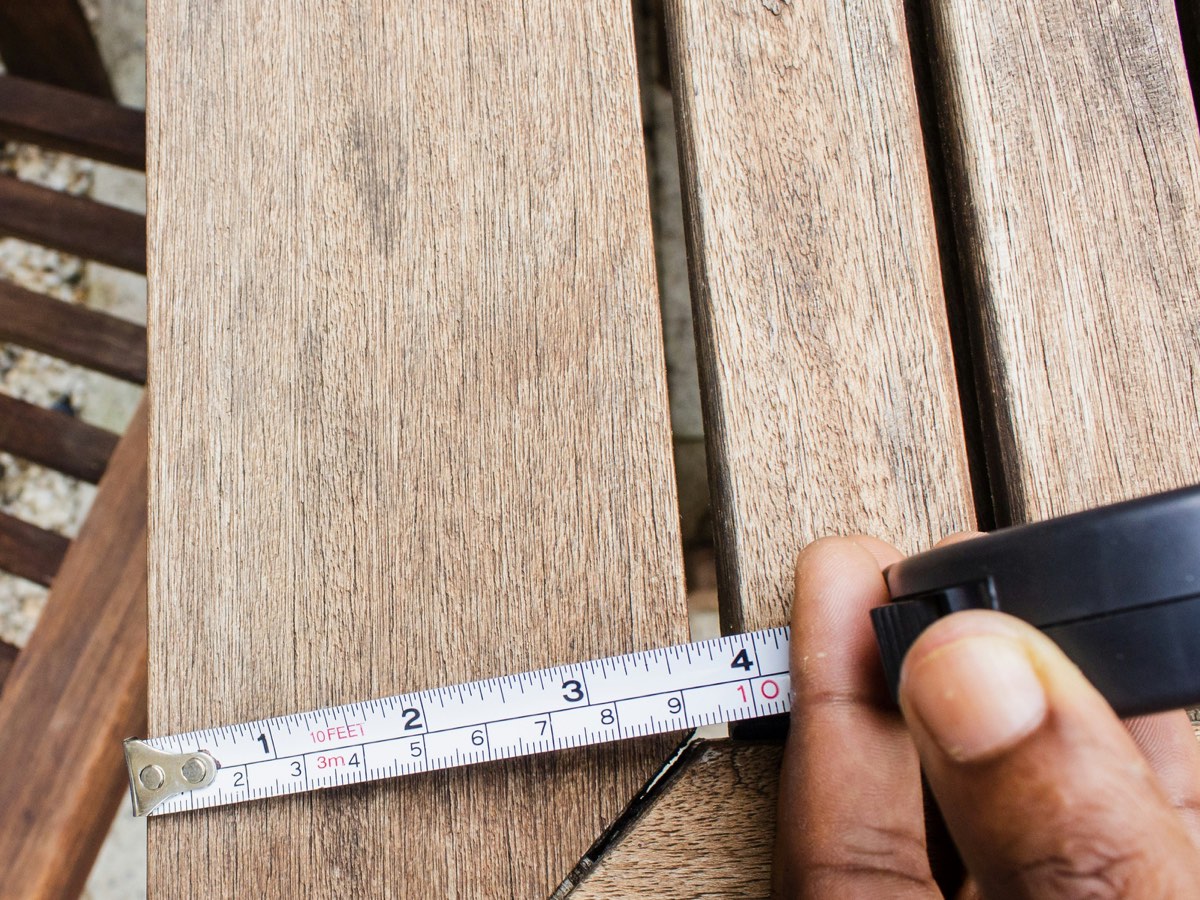 A hand pulling a tape measure across a wood plank.